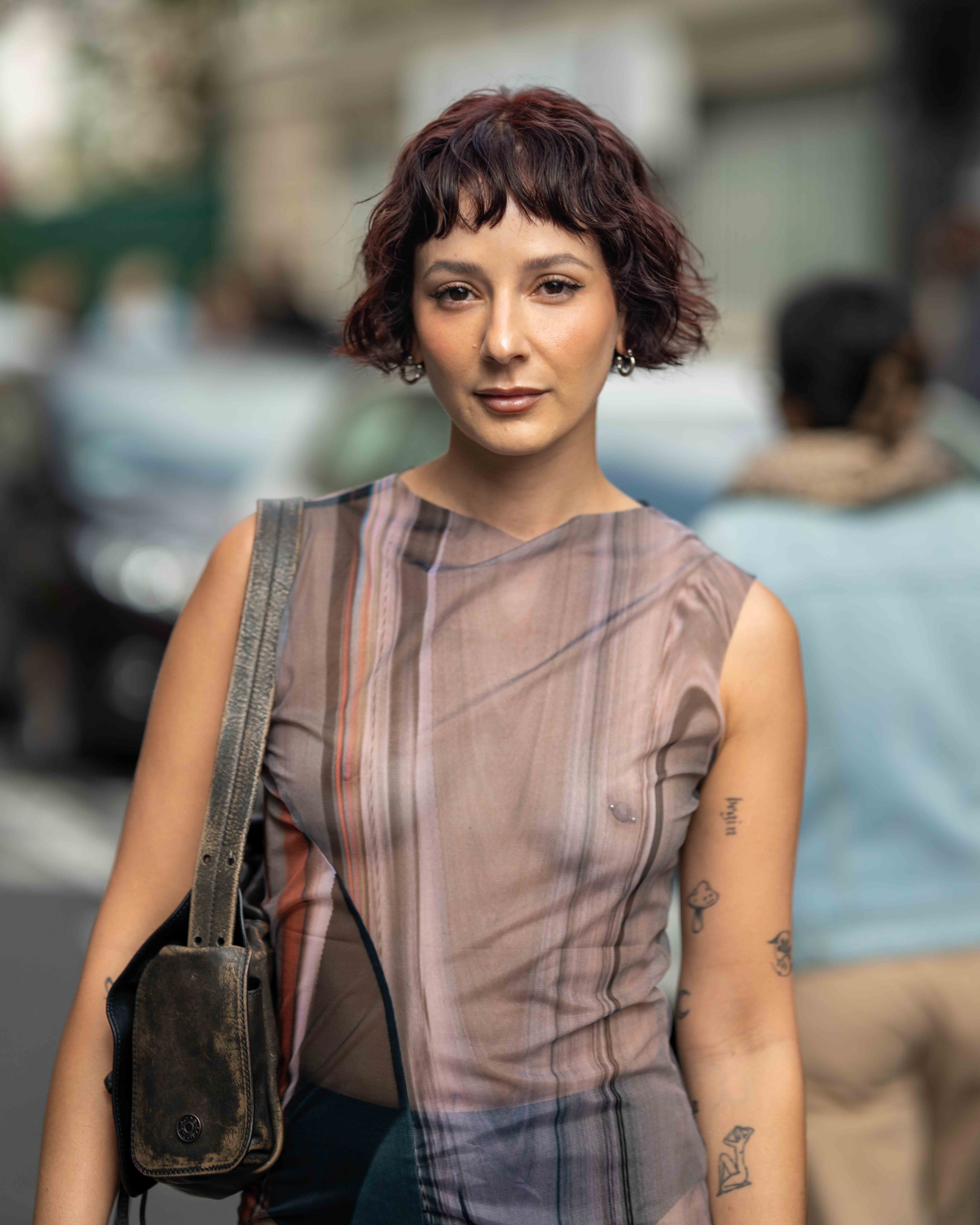 A guest wears a see through striped dress without a bra, with a pierced nipple. Street Style before Issey Miyake Paris Fashion Week SS24