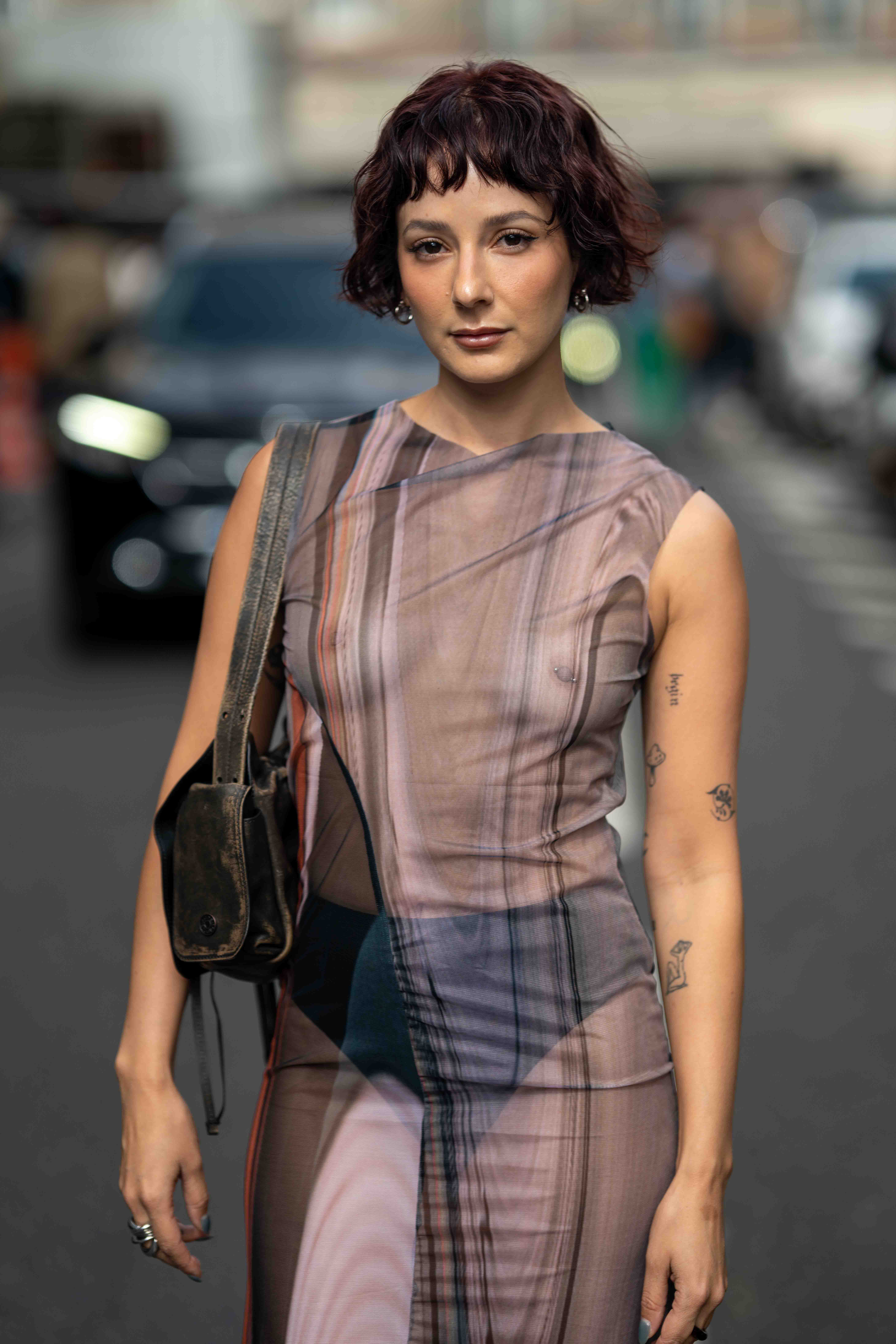 A guest wears a see through striped dress without a bra, with a pierced nipple. Street Style before Issey Miyake Paris Fashion Week SS24
